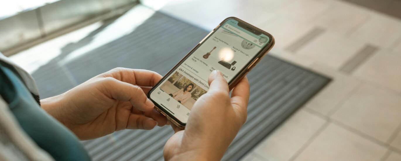 Close-up of hands holding a smartphone displaying an online shopping app in an indoor setting.