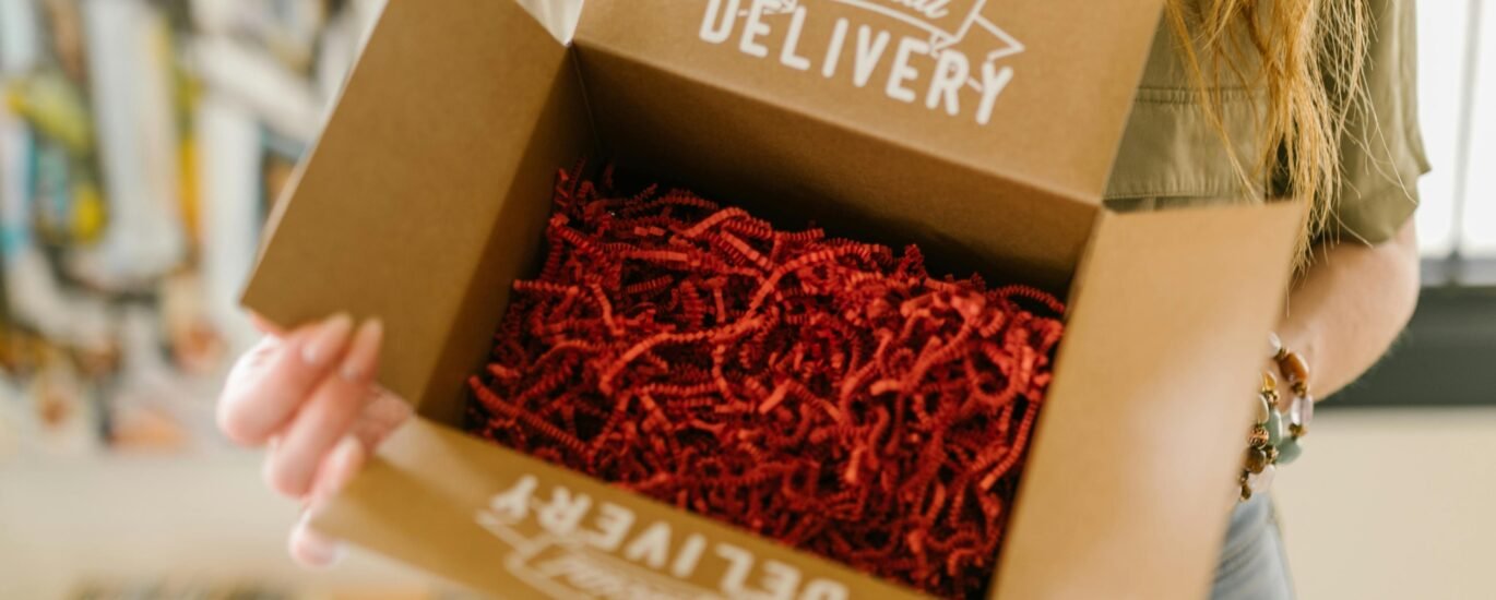 Person opening a special delivery box filled with red crinkle paper for secure packaging.