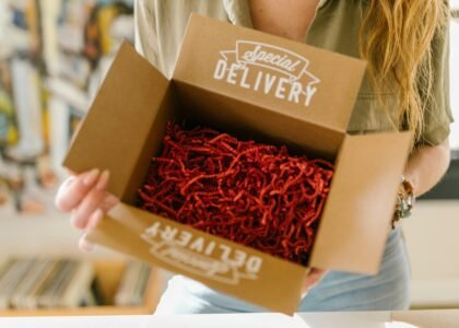 Person opening a special delivery box filled with red crinkle paper for secure packaging.